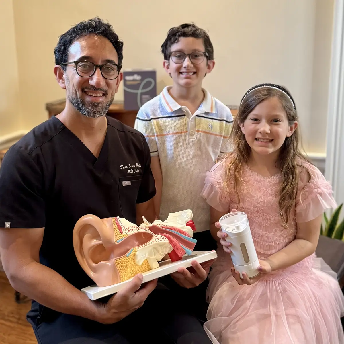 Healthcare professional holding an ear model and earflo device sitting with two children