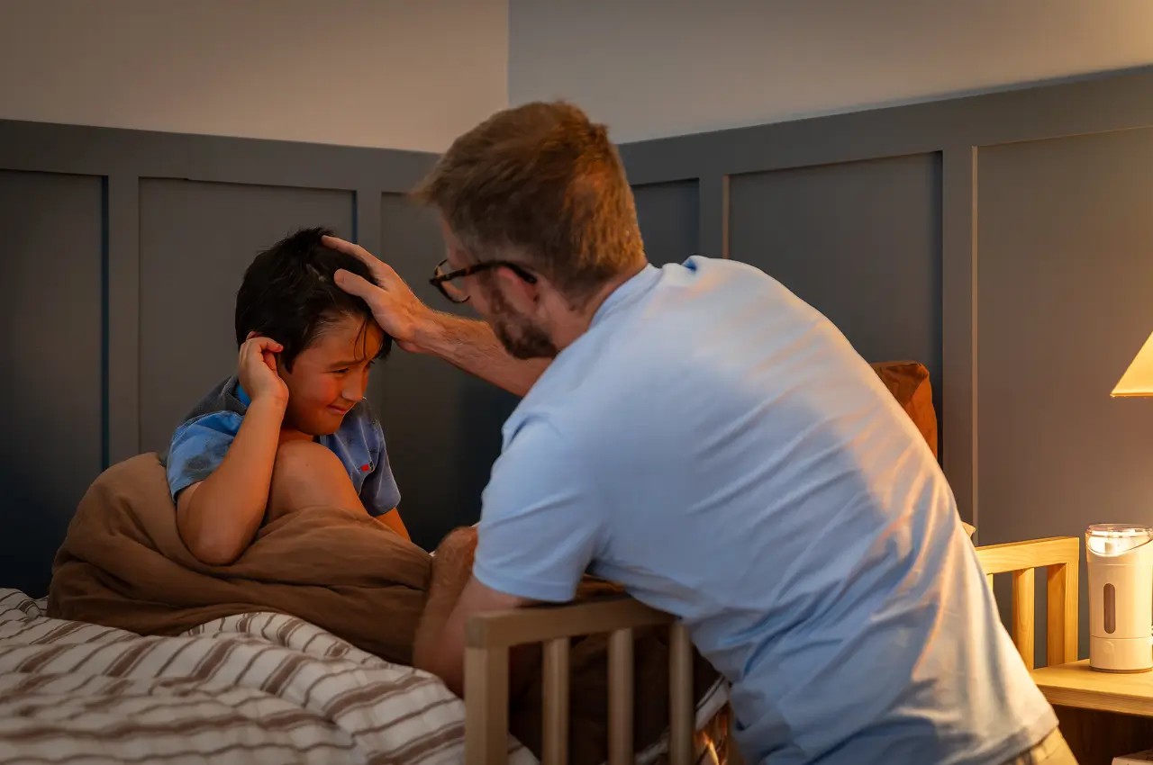 Adult comforting a child sitting in bed with hands over their ears