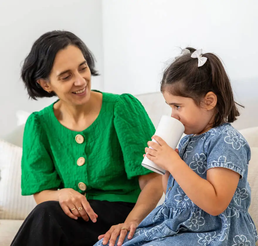 Parent sitting next to child while child drinks from the Earflo device like a sippy cup
