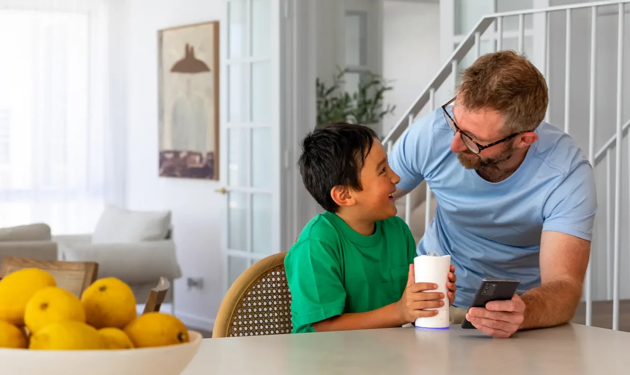 Parent smiling with a child at a table while the child holds the Earflo device